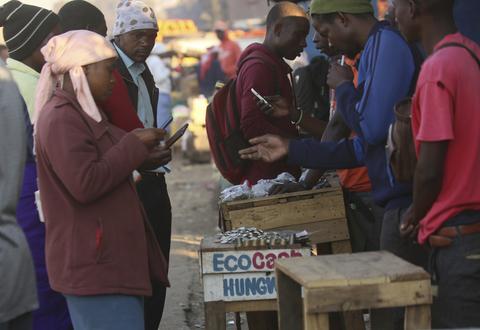 Vendors are seen on their mobile phones while selling cash at a premium in Harare, Zimbabwe. Picture: AP Photo/Tsvangirayi Mukwazhi